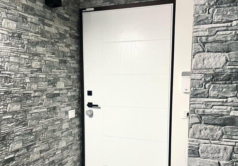 Porta blindata bianca con pannello liscio su parete in pietra